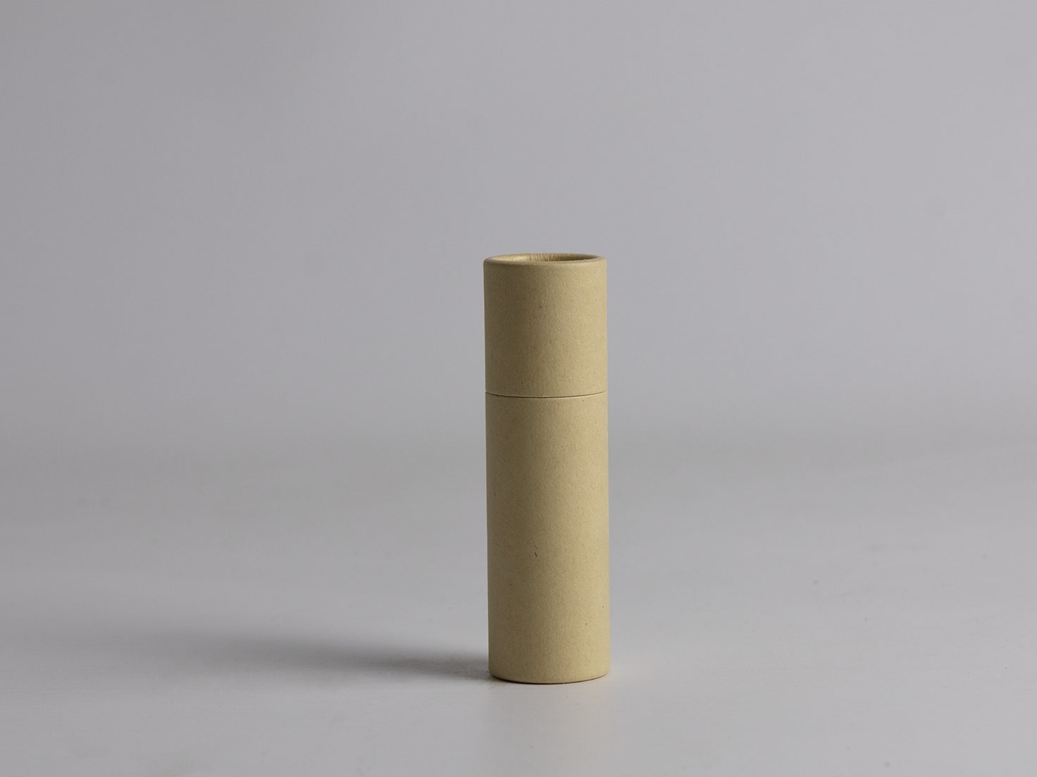 Beige cardboard push tube with bottom-push mechanism for easy dispensing of natural lip balms, sunscreens, and solid cosmetics. Eco-friendly, minimalist skincare packaging with sustainable design on soft gray background.